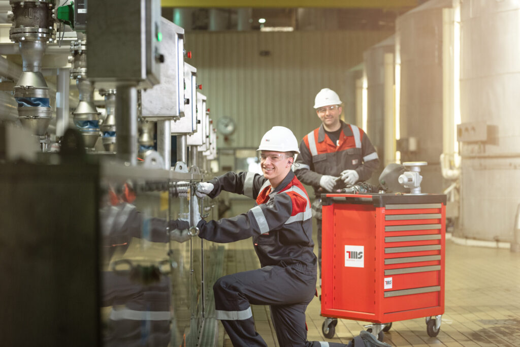 Twee techniekers met pbm's voeren onderhoud uit aan een industriële installatie.